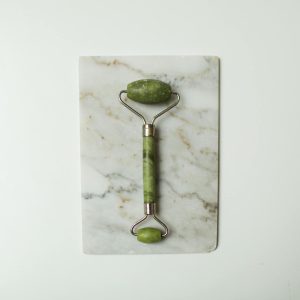 Close-up of a jade face roller on a marble slab, ideal for skincare and facial massage routines.