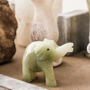 Decorative green jade elephant figurine displayed among ceramic and stone vases indoors.